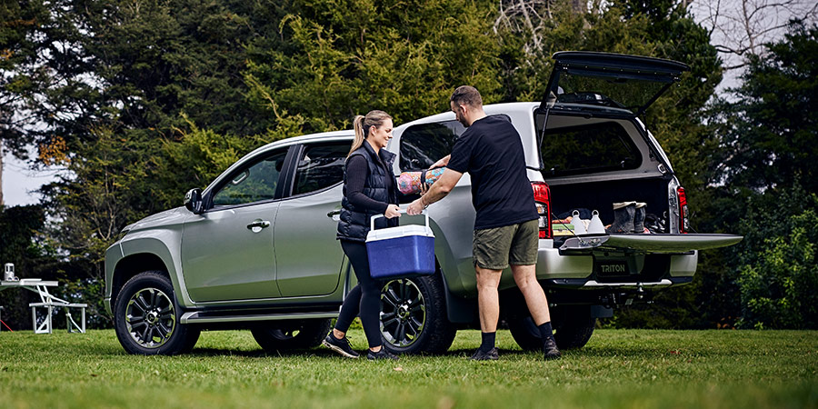 A man handing a woman a cooler infront of a ute with the boot open