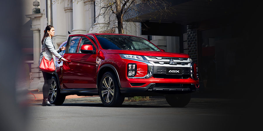 A small red Mitsubishi SUV parked in s a street, with a woman getting in the drivers side door