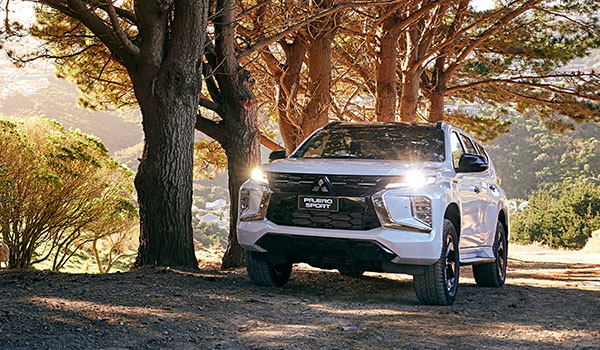 A white SUV with lights on driving on a road next to a forest at sunset